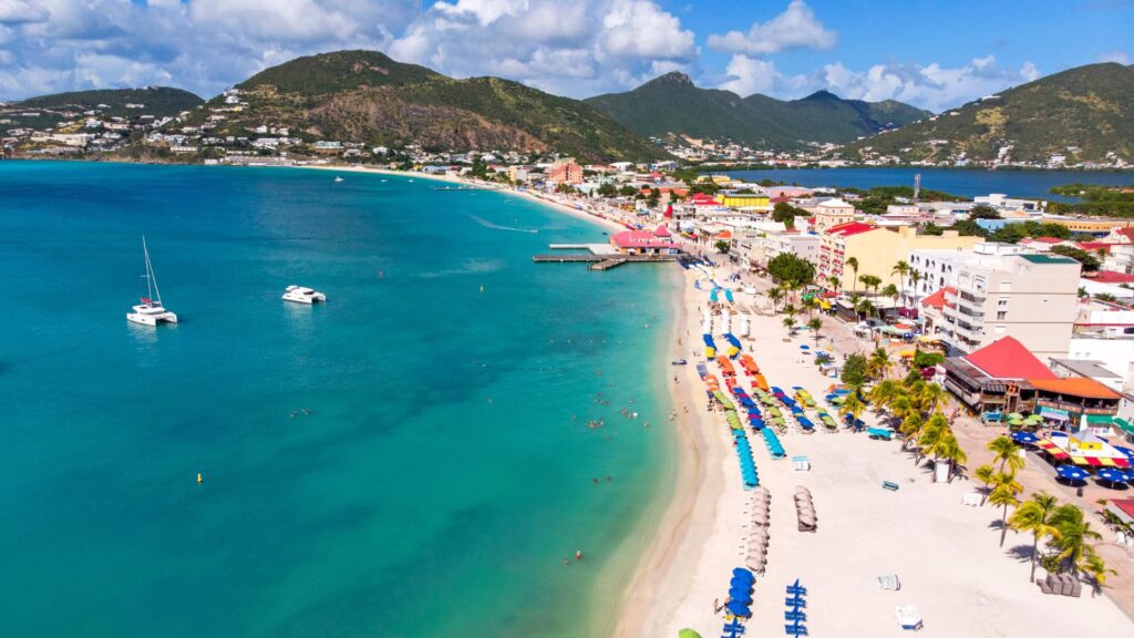 Helicopter flying above Grreat Bay Beach, Philipsburg with turquoise Caribbean waters below in St. Maarten.